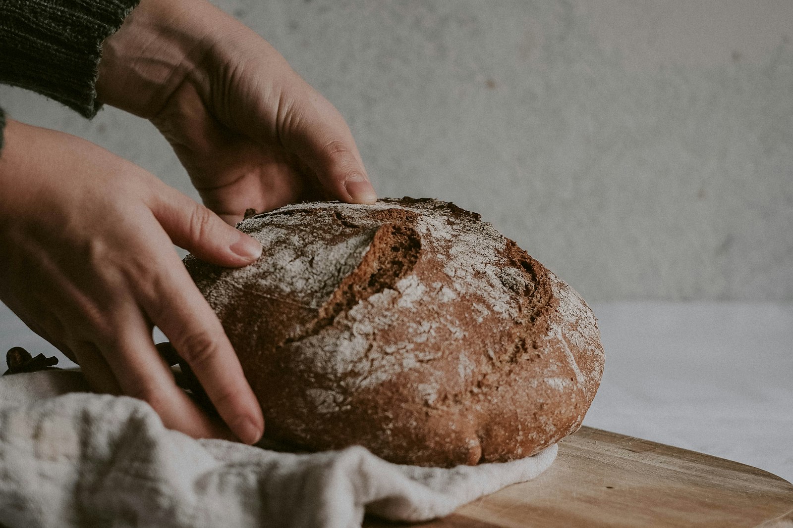 Hands holding a fresh loaf of brown bread on a wooden board