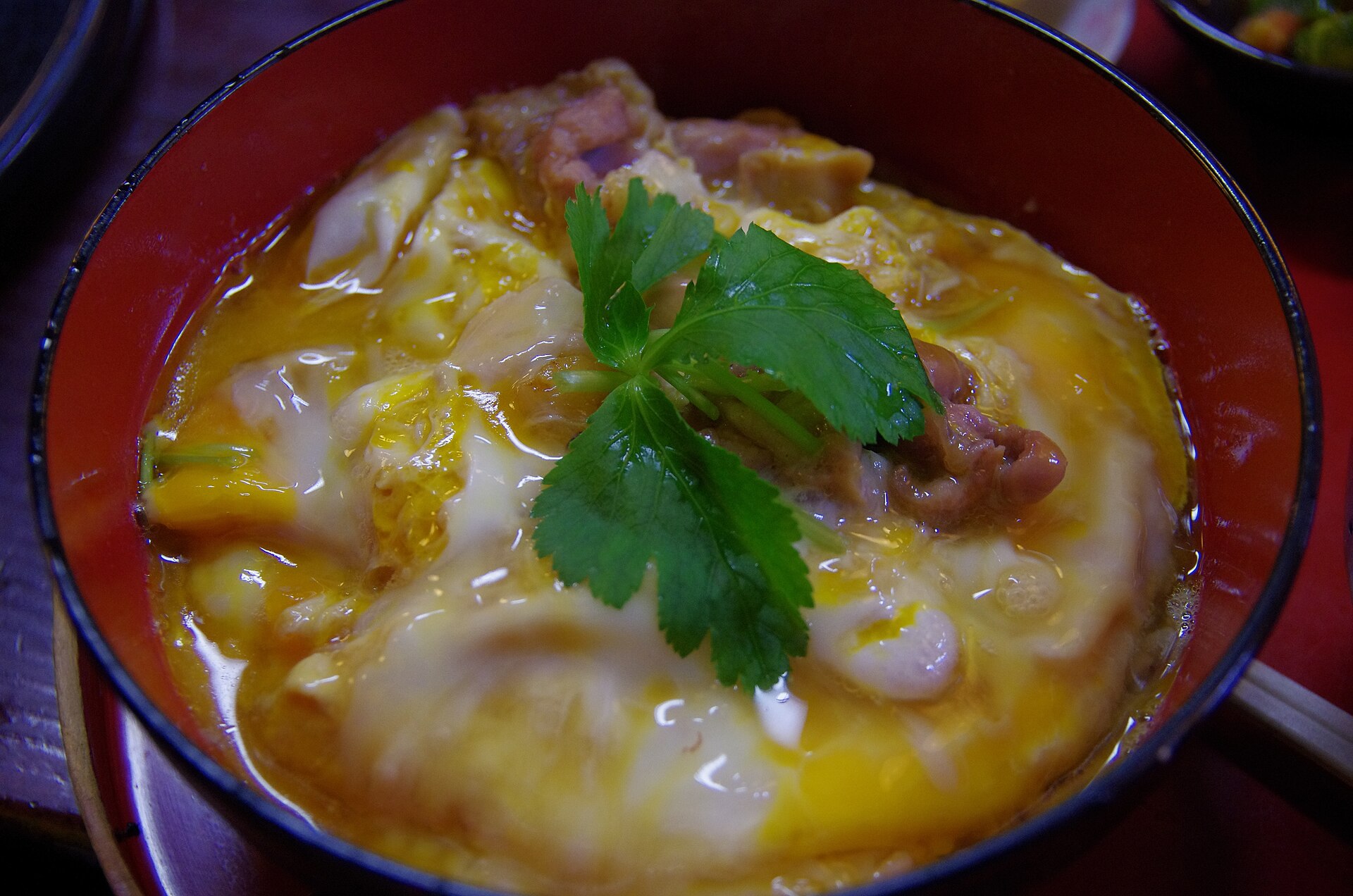 A bowl of white rice topped with sliced browned chicken thigh, herbs and pickled onion