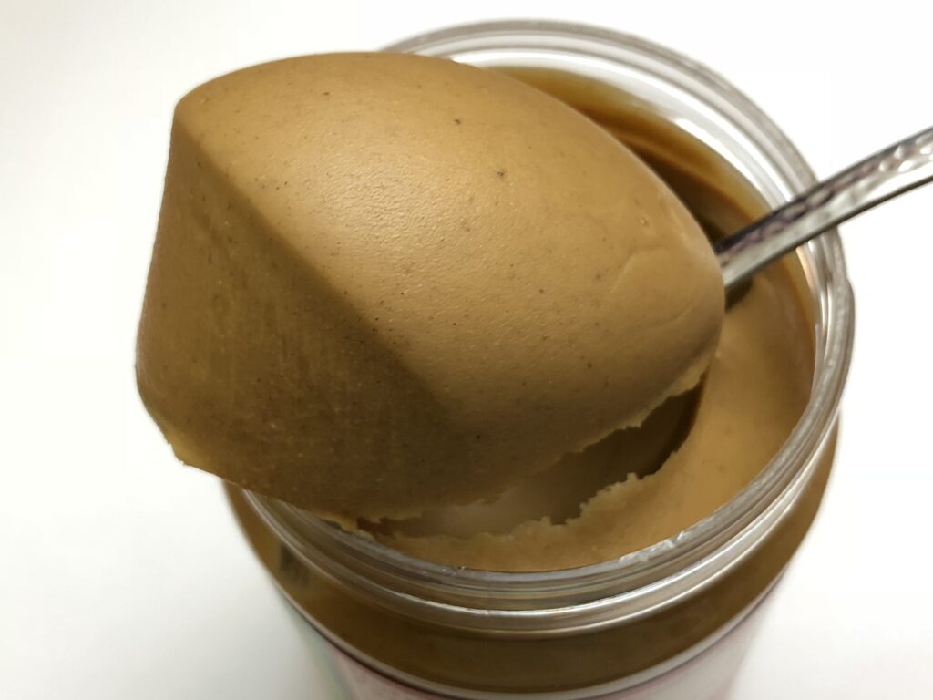 An open jar of peanut butter with a spoon resting beside soy sauce and a lime