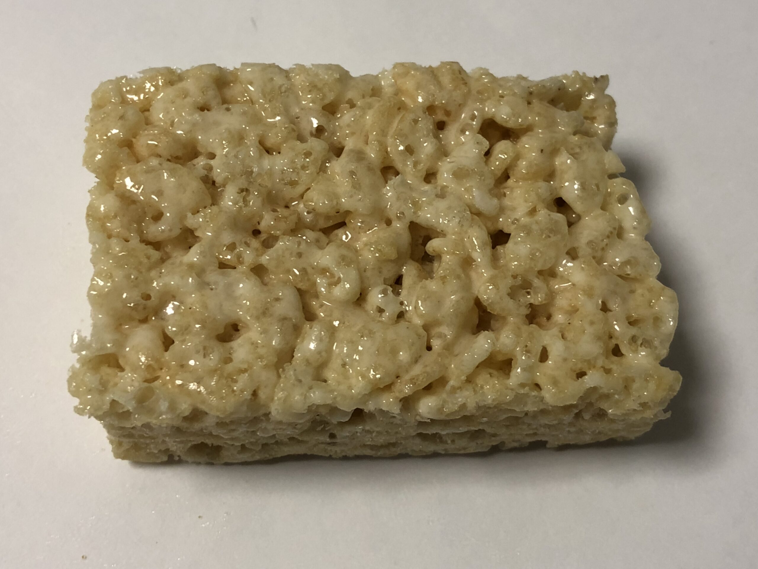 Cut squares of golden crisped rice and marshmallow treats stacked on a sheet of parchment