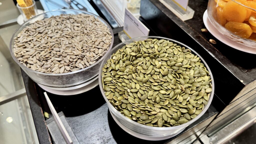 Green pumpkin seeds and dried cherries in small bowls on a wooden counter