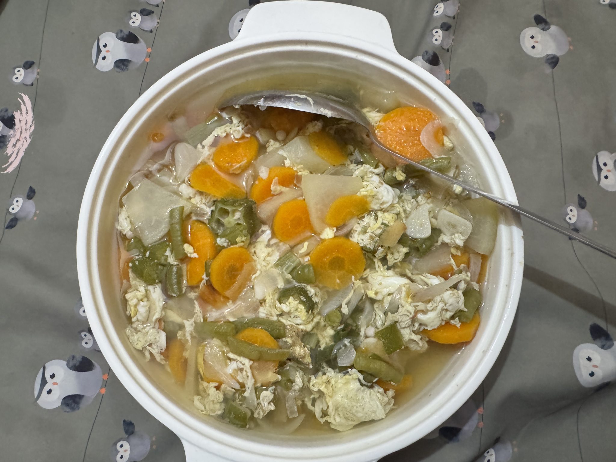 A white bowl of clear soup with pale egg ribbons and sliced green scallions on top