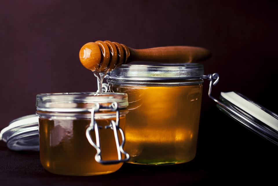 A glass jar of honey with a spoon drawing a thin thread of it upward