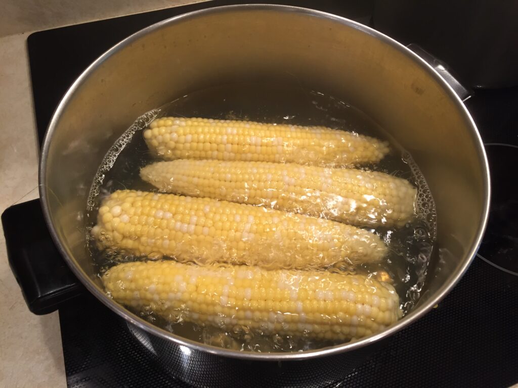 Shucked ears of corn boiling in a large stockpot of water on the stove