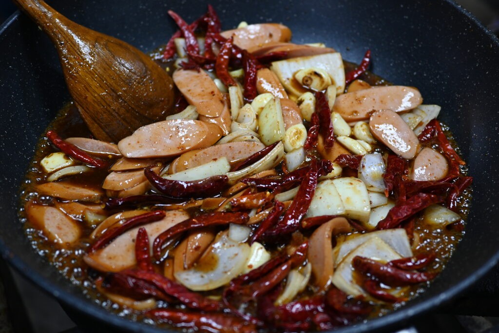 Crumbled sausage meat browning in a wide skillet with a wooden spoon resting in it