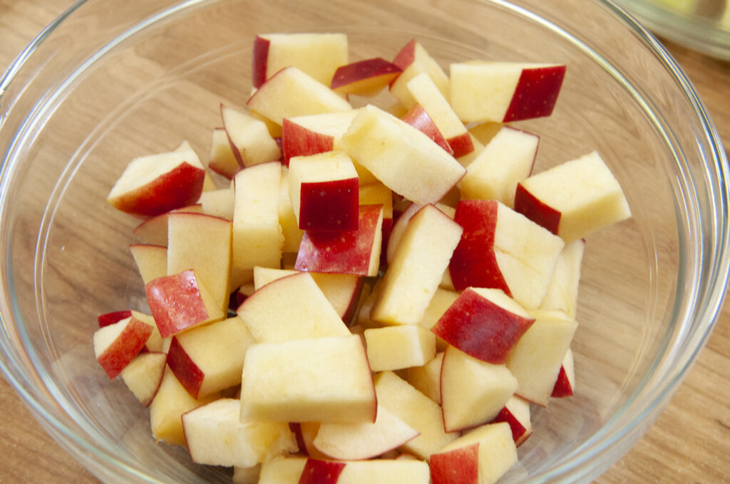 Peeled apples cut into small cubes piled in a glass bowl beside a paring knife
