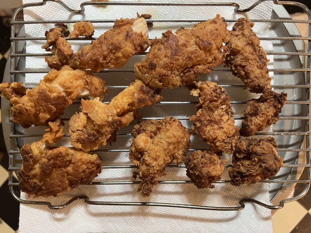 Pieces of bone-in fried chicken with craggy golden coating resting on a wire rack