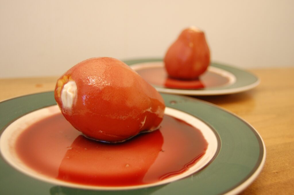 Whole peeled pears simmering upright in dark liquid in a wide saucepan