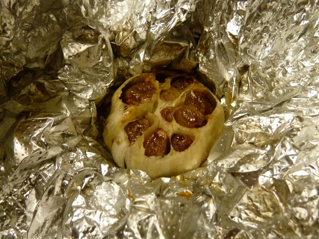 A roasted head of garlic opened to show soft browned cloves beside a small dish