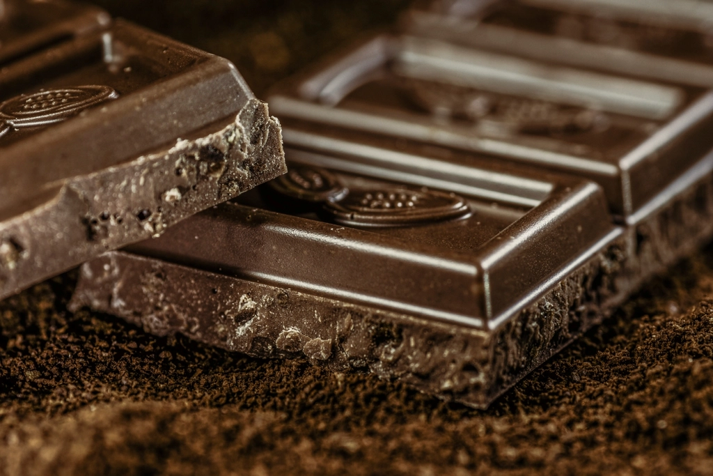 A broken bar of dark chocolate in rough pieces on a pale marble surface