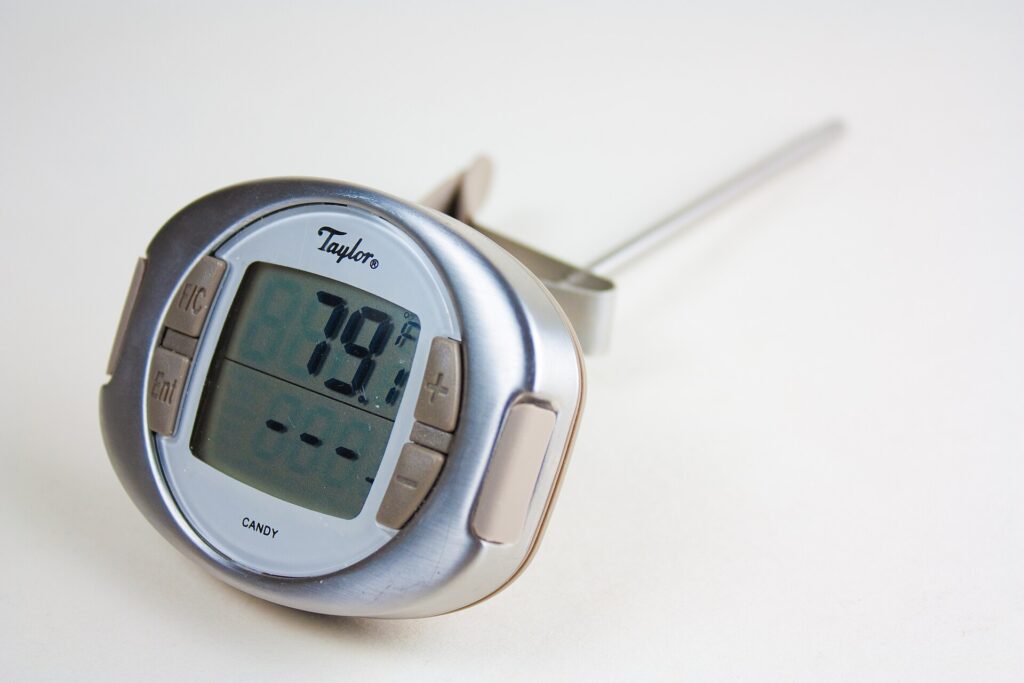 A candy thermometer clipped to a saucepan of bubbling amber sugar syrup on a stove