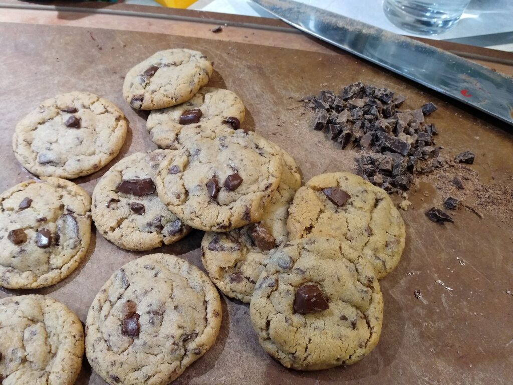 Freshly baked chocolate chip cookies cooling in rows on a metal baking tray