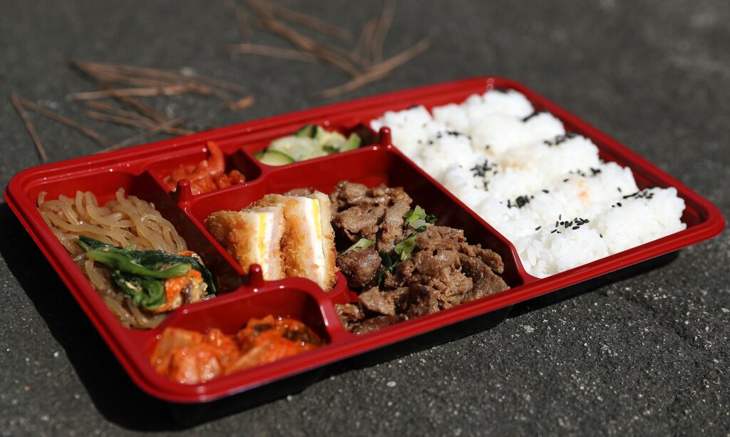 A small sealed container of hummus packed next to sliced vegetables in a lunchbox