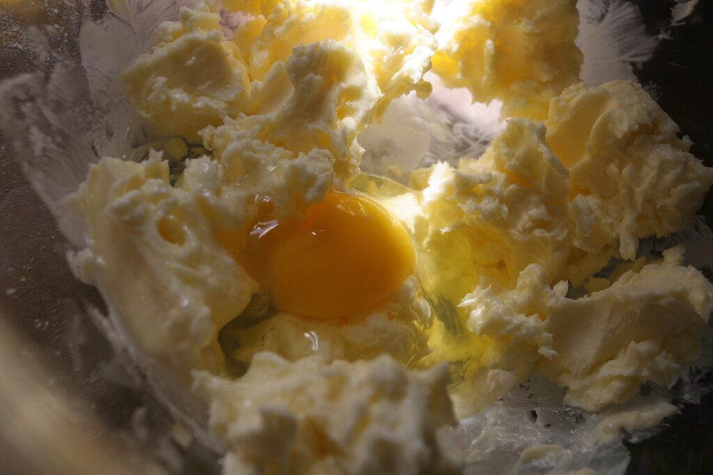 A single raw egg yolk sitting in a small glass bowl beside a cracked eggshell