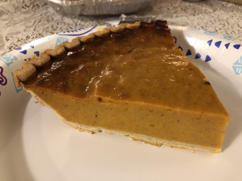A single slice of baked pumpkin pie with a dollop of whipped cream on a white plate