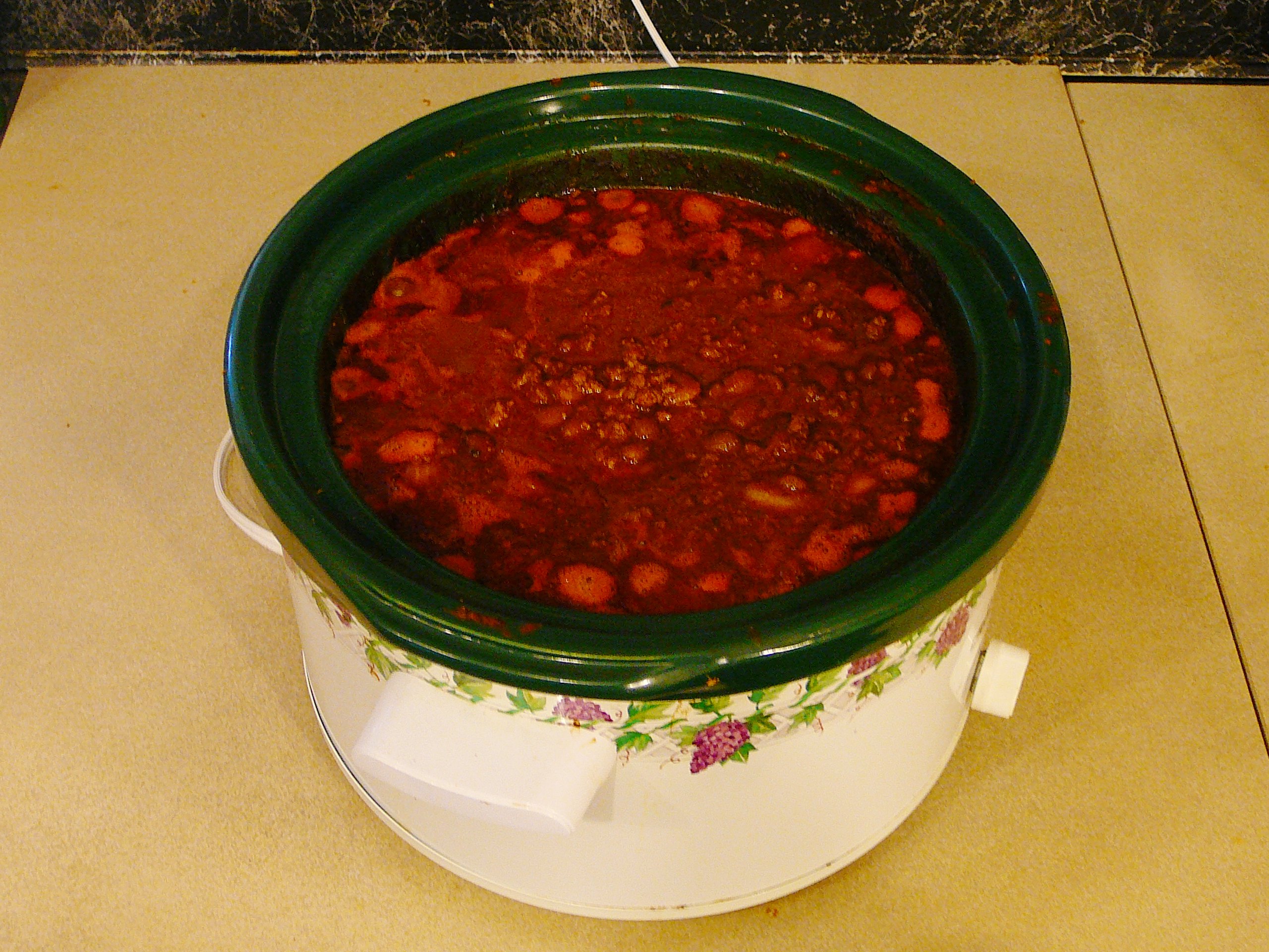 A heavy pot of thick chili with beans and ground meat, wooden spoon resting in it