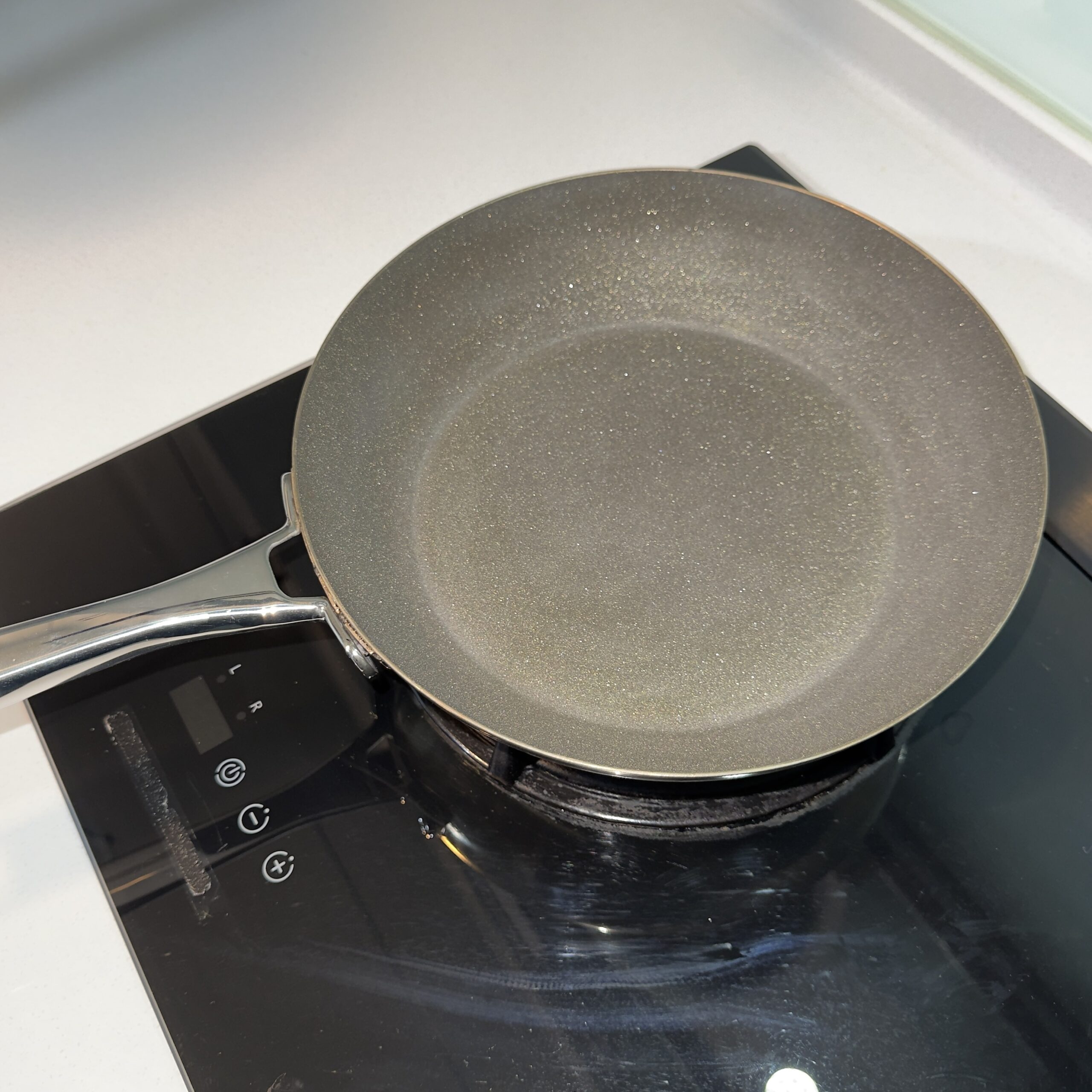 A black coated skillet on a stovetop with a wooden spatula resting across the rim