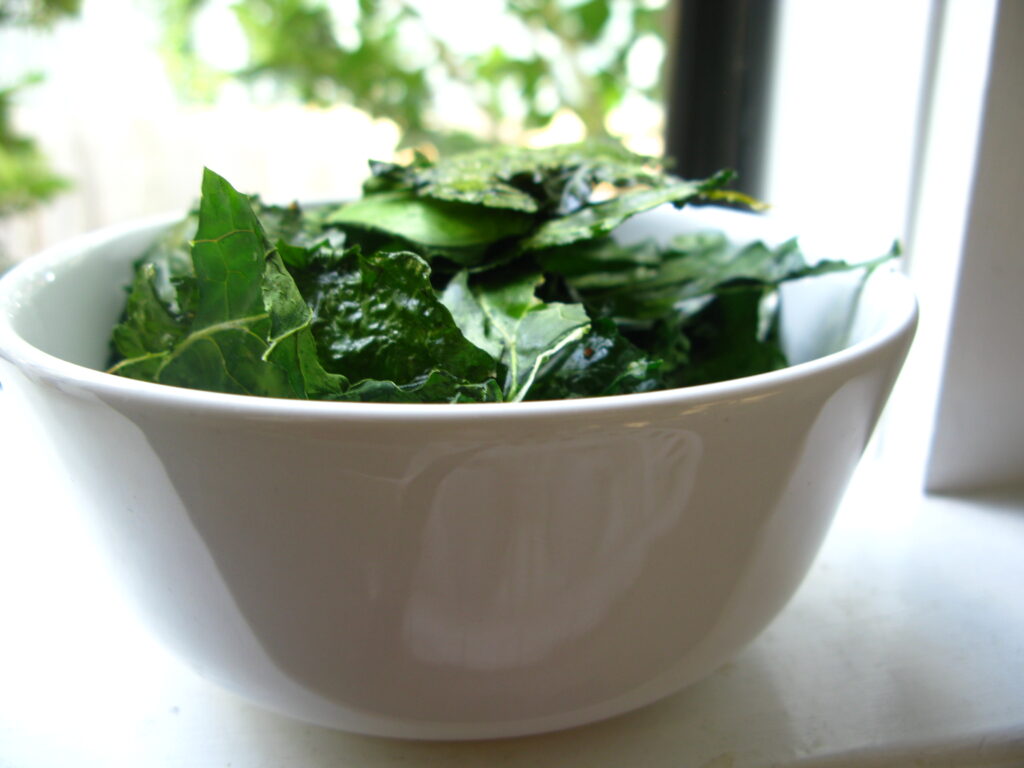 Torn kale pieces spread in a single layer across a parchment lined sheet pan