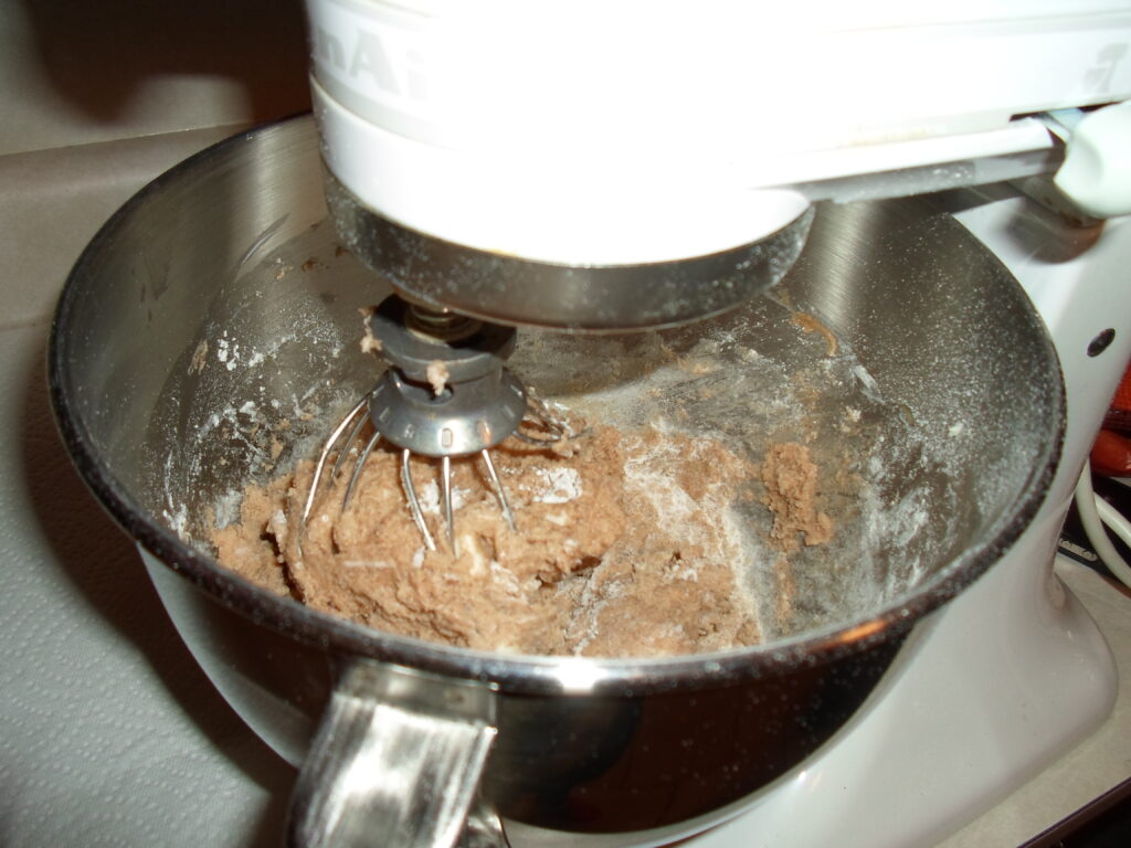 A stand mixer with a paddle attachment beating pale butter and sugar in a metal bowl