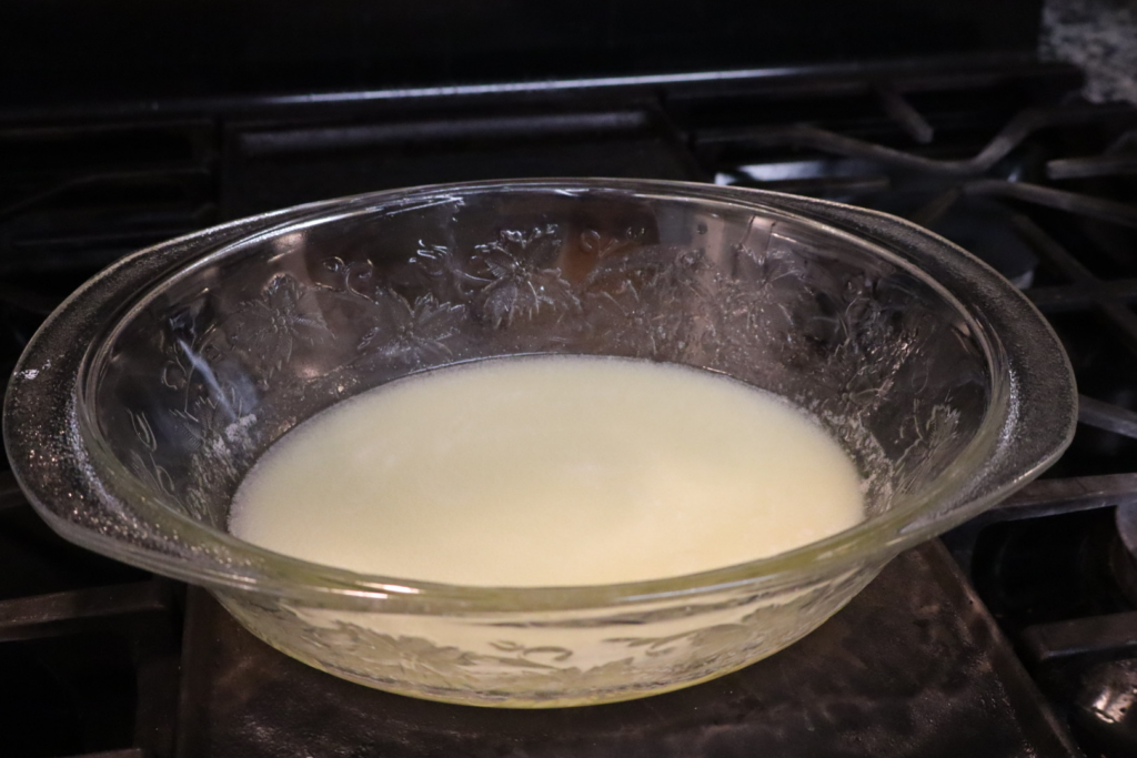 Golden melted butter being poured from a small saucepan into a mixing bowl