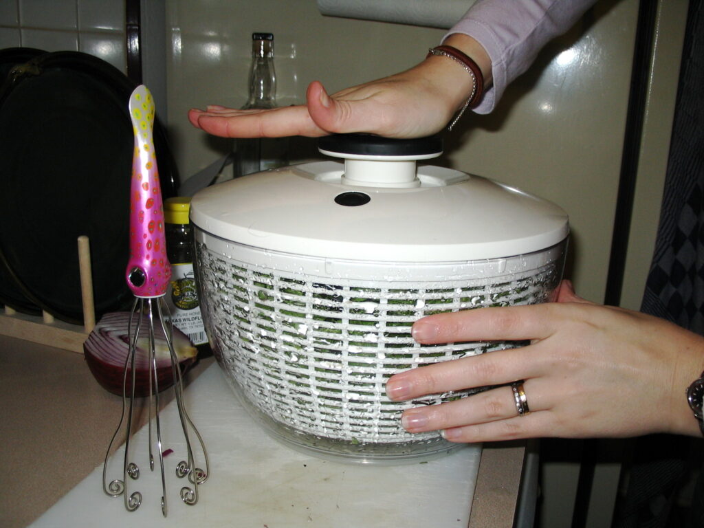 A salad spinner filled with washed green leaves standing beside a kitchen sink