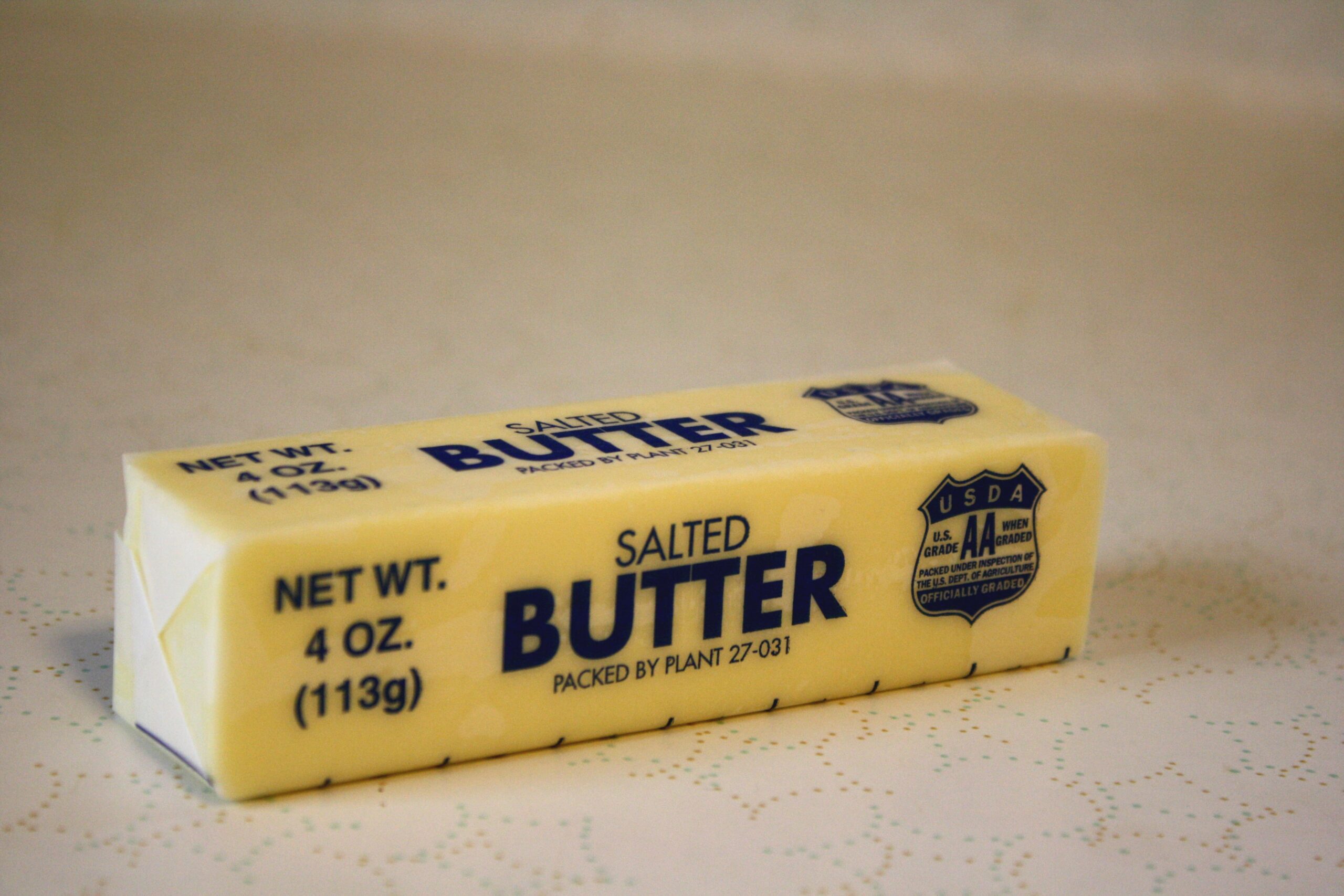 A stick of butter on a wooden board with a knife and a probe thermometer