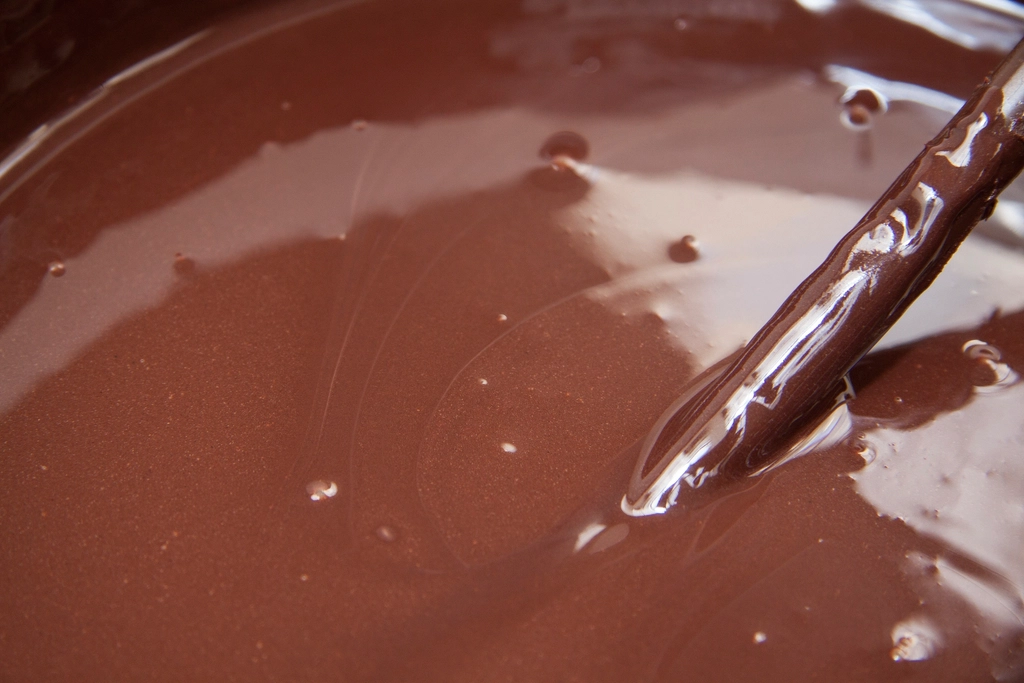 Glossy melted dark chocolate being stirred with a spatula in a dry glass bowl