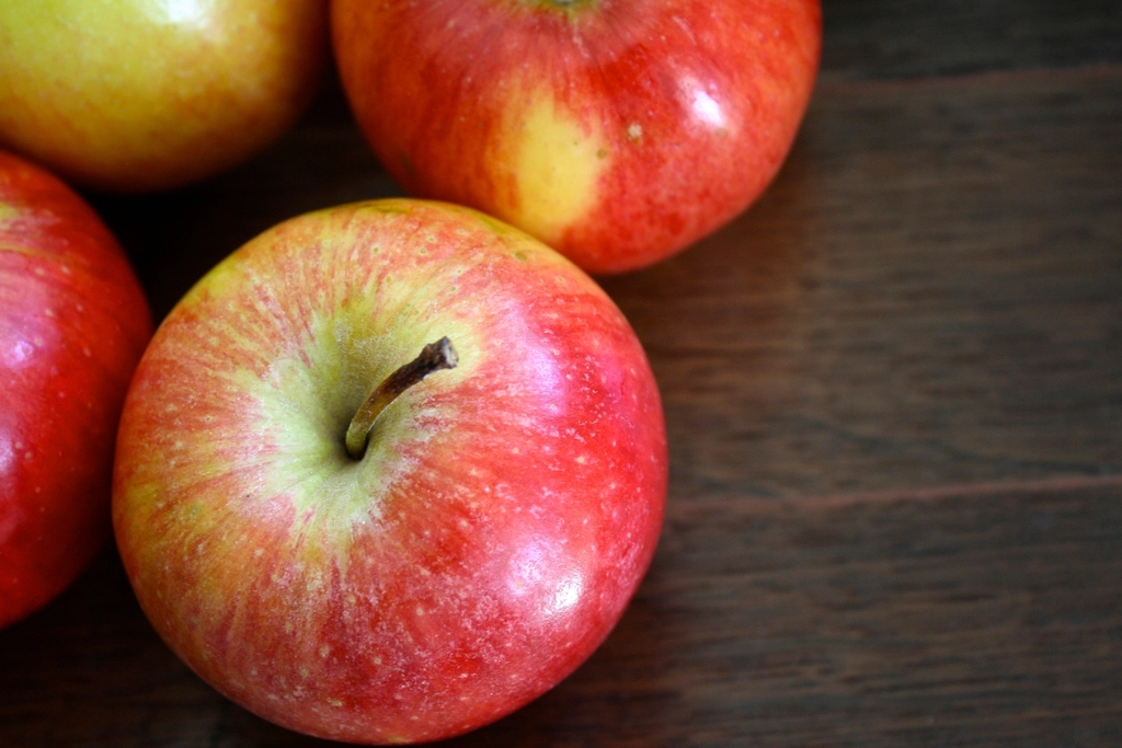 Several whole red and green apples resting on a plain wooden kitchen table